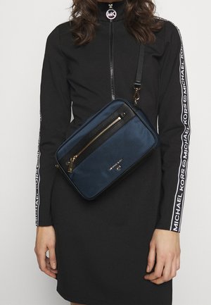 Navy crossbody bag with a textured finish, featuring a gold zipper, a black trim, and the brand name embossed on the front.