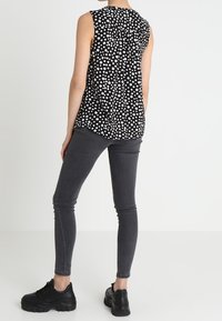 Černý top bez rukávů s bílými puntíky, v kombinaci s úzkými tmavě šedými džínami. Obuv tvoří robustní černé tenisky.