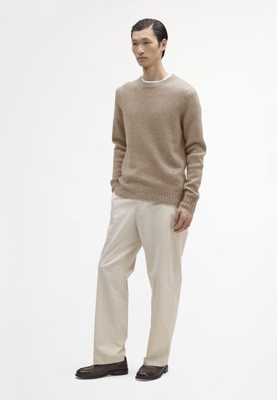 Beige gebreide trui, ronde hals, textuurstof met geribde manchetten en zoom. Gecombineerd met crèmekleurige, relaxed-fit broeken en donkere instappers.