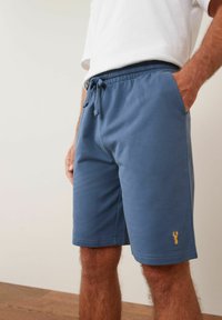 Blaue Baumwollshorts mit elastischem Bund und Kordelzug, versehen mit einem kleinen gelben Hummerdesign am unteren Saum. Glatte Textur, lässiger Schnitt.