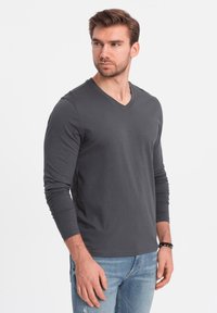 Graues Langarm-V-Ausschnitt-Shirt aus weichem Material, mit passgenauer Schnittführung und glatter Textur, kombiniert mit hellblauen, verwaschenen Jeans.