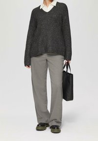 Sort, glitrende sweater med v-udskæring; lysegrå, løstsiddende bukser; sort håndtaske med håndtag; kraftige sorte og grønne sko.