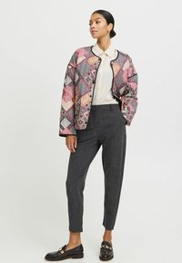 Veste matelassée avec un design rose et à motifs, bord noir ; associée à un pantalon gris ajusté et des mocassins avec des accents en métal doré.