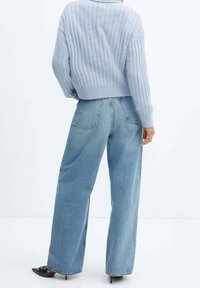 Helles blaues, geripptes Sweatshirt mit hohem Kragen, kombiniert mit hoch taillierten, weiten hellblauen Jeans und schwarzen spitzen Pumps.