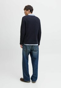 Dark ribbed sweater with light blue collar, paired with loose-fitting faded blue jeans and brown shoes, viewed from the back.