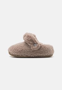 Luddig beige toffel med rund tå och ett justerbart spänne. Tillverkad av mjukt tyg med en texturerad, plyschyta, med en cirkulär logotypaccent.