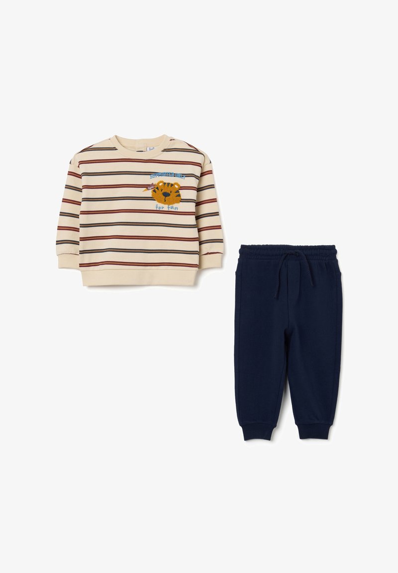Felpa beige a righe con pantaloni blu navy. La felpa presenta righe orizzontali rosse e blu e un'illustrazione di una tigre con del testo. I pantaloni hanno una vita elastica.