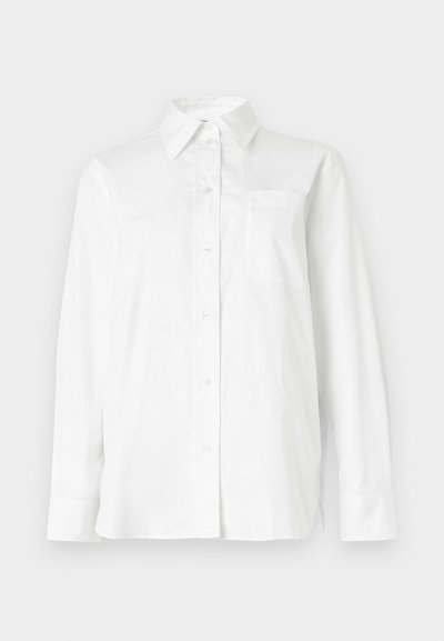 Λευκό πουκάμισο με μακριά μανίκια, κουμπιά μπροστά, με μυτερό γιακά και τσέπη στο στήθος, τοποθετημένο επίπεδα πάνω σε ανοιχτό φόντο.