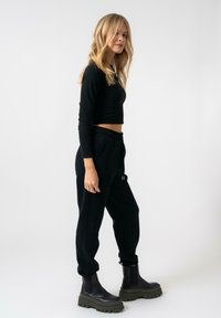 Top corto nero e pantaloni jogger neri con vita elasticizzata. Stivali neri a suola spessa con accenti verdi. Design semplice e aderente.
