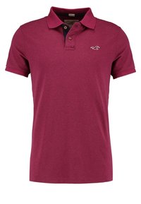 Burgundyröd polo skjorta tillverkad av mjukt tyg, med en klassisk krage, tre knappslå och en diskret logotyp på bröstet.