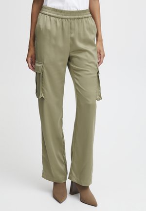 Pantalons cargo satin vert olive avec poches latérales, taille élastique et coupe droite, associés à des chaussures à talons hauts marron clair.
