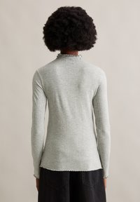 Helles graues, geripptes Langarmoberteil mit einem Rüschkragen, taillierter Passform und einem rohen Saum am unteren Ende. Glatte Textur, elastischer Stoff.