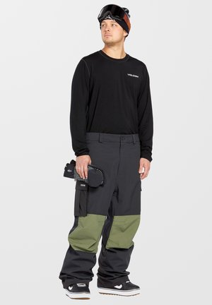 Conjunto de snowboard que incluye una camiseta negra de manga larga y pantalones negros holgados con puños verdes. Incluye unas gafas de esquí y un accesorio texturizado.