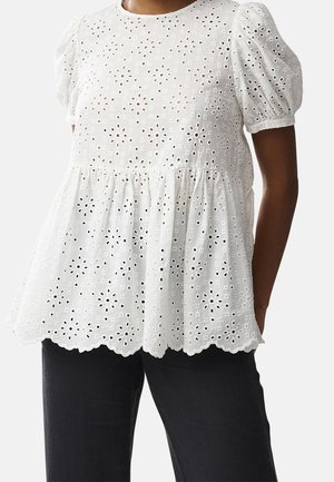 Weiße Ösen-Spitzenbluse mit Puffärmeln und geschwungenem Saum, getragen zu schwarzen Hosen.
