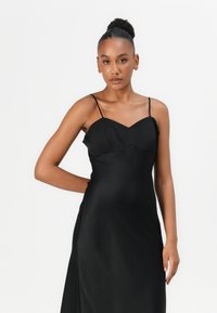 Black satin dress with spaghetti straps, featuring a V neckline and a smooth, flowing design. The fabric has a soft, glossy texture.