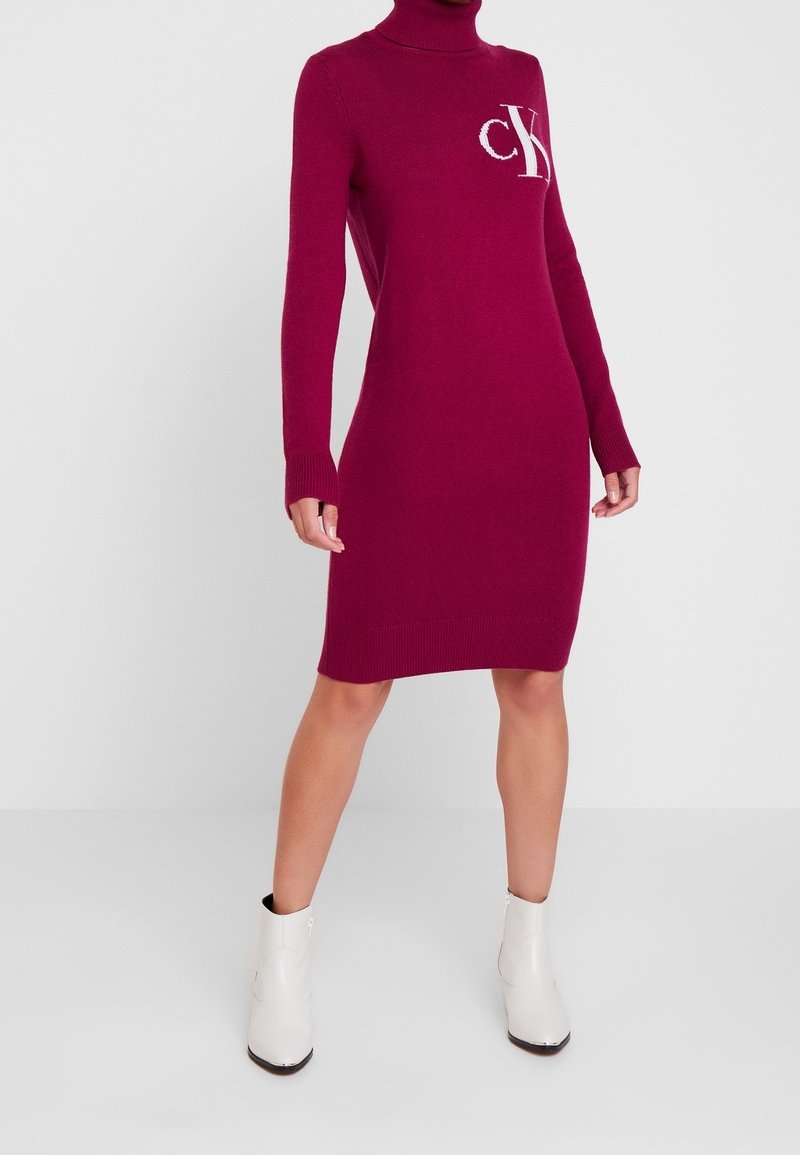 Figurformad magenta polotröja med långa ärmar, med en vit CK-logotyp på bröstet. Mjuk stickad textur, knä-length design.