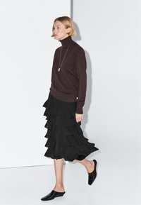 Brown turtleneck sweater, black ruffled skirt, and black slip-on shoes. Smooth texture, layered design in skirt, and elongated fit on top.