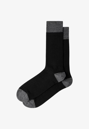 Par de calcetines negros de caña con puños, talones y punteras grises, dispuestos planos y superpuestos sobre un fondo blanco.