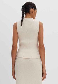 Top senza maniche a coste beige con una linea diritta. Presenta un collo alto e una texture sottile, che completa una silhouette aderente.
