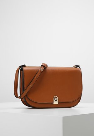 Bruine leren crossbodytas met verstelbare band en gouden gesp, rustend op een wit oppervlak tegen een effen achtergrond.