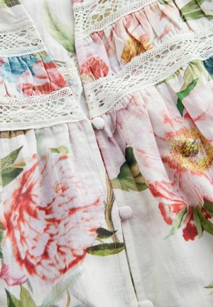 Látka s květinovým vzorem, na které jsou růžové a červené květiny na světlém pozadí. Obsahuje bílou krajku a malé kulaté knoflíky. Měkká textura.