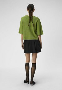 Haut vert à manches courtes côtelé, jupe plissée noire, chaussettes noires transparentes jusqu'aux genoux et chaussures à petit talon. Design simple, silhouette ajustée.