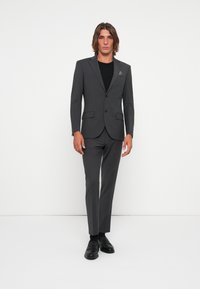 Gray suit with single-button blazer, matching slim trousers, and black shirt underneath. Smooth fabric with minimalistic design and no visible patterns.
