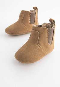 Bløde brune suede babystøvler med scallopede kanter, elastiske sidepaneler og fuzzy inderside, præsenteret på en hvid baggrund.