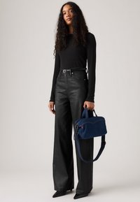 Top negro de manga larga y jeans negros de tiro alto y pernera ancha. Bolso de mezclilla azul con asas cortas y correa de hombro desmontable.