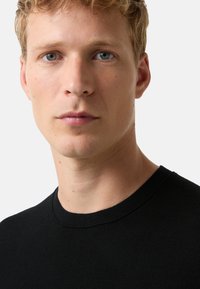 Czarna bawełniana koszulka typu crewneck z teksturowaną powierzchnią, z okrągłym dekoltem i dopasowanym krojem. Minimalistyczny i uniwersalny styl.