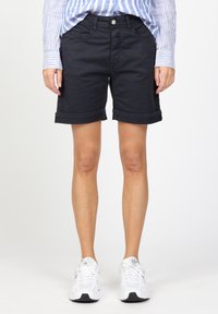 Tmavě modré bavlněné šortky s ohrnutými lemy, kapsami vpředu i vzadu a zapínáním na knoflík, doplněné bílými sportovními botami a modrým pruhovaným tričkem.