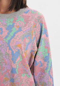 Sweat-shirt gris avec un motif abstrait coloré en rose, vert, bleu et orange. Texture douce avec un col rond et des manches longues.
