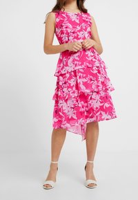 Pink floral dress with a layered design, featuring ruffled tiers. Made of lightweight fabric, has a boat neckline and an asymmetrical hem.