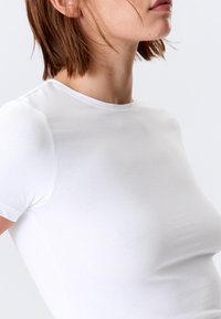 T-shirt blanc ajusté en coton lisse, avec un col rond classique et des manches courtes. Design minimaliste sans motifs visibles.