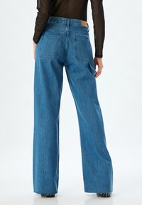 Jeans de mezclilla azul de pierna ancha con cintura alta, que presentan bolsillos traseros, una etiqueta de cuero en la cinturilla y una textura deslavada.