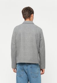 Grijze geruite jas met een gestructureerde kraag, voorzien van een textiele stof, aangepaste pasvorm en rechte zoom. Draag het over denim jeans.