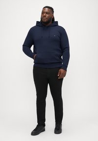 Granatowa bluza z kapturem z miękkiego materiału, z przednią kieszenią i sznurkiem do regulacji, w zestawieniu z czarnymi slim fit dżinsami i czarnymi tenisówkami.