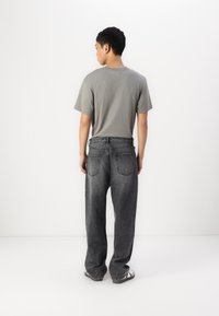 Gray T-shirt, black denim jeans with a loose fit, five pockets, elastic waistband, worn with black-and-white sandals, viewed from the back.