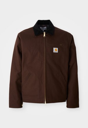 Brown canvas jacket featuring a gold zipper, corduroy collar, left chest pocket with logo patch, and side pockets with concealed zippers.