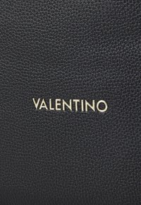 Črna teksturirana usnjena torba z zlatim logotipom "VALENTINO", poudarja kamenčkast površin in eleganten dizajn.