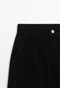 Pantalons en velours côtelé noir présentant une surface texturée, des côtes verticales, des poches standard et un bouton en métal à la taille.