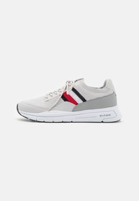 Chaussure de sport légère avec un dessus en tricot beige, des accents gris et un détail rayé rouge et marine. Elle possède une semelle blanche rembourrée.