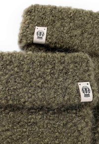 Grüner, texturierter Wollstoff mit fuzzy Erscheinung. Besitzt ein kleines Lederetikett mit einem gedruckten Design. Zwei überlappende Stücke sind abgebildet.