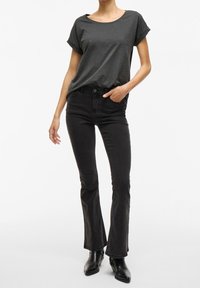 T-shirt gris à manches courtes associée à un jean noir évasé taille haute. Mannequin portant des bottines noires ; tissu lisse et coupe ajustée.