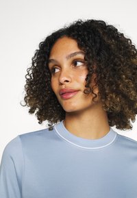  Lichtblauwe longsleeve shirt met een ronde hals en witte accenten. De stof is soepel en de pasvorm is casual, wat mooi aansluit bij krullend haar.