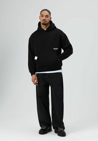 Zwart hooded sweatshirt met een voorzak, geribbelde boorden en logodetail. Gecombineerd met losse zwarte spijkerbroek en zwarte veterlaarzen.