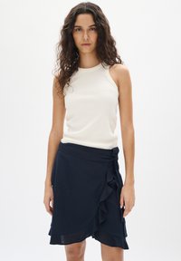 Krém színű, bordázott tank top, ami egy tengerészkék, fodros szegélyű, megkötős derék részletes szoknyával van párosítva.