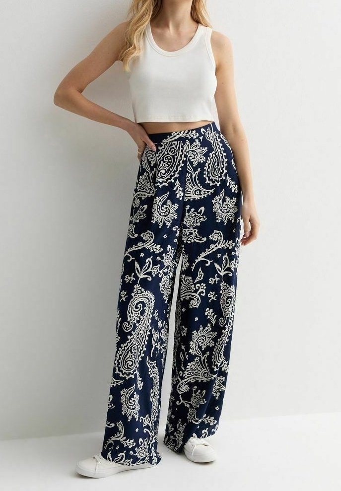 Pantalon large marine avec un motif paisley blanc, en tissu léger. Associé à un débardeur court blanc et des chaussures blanches.