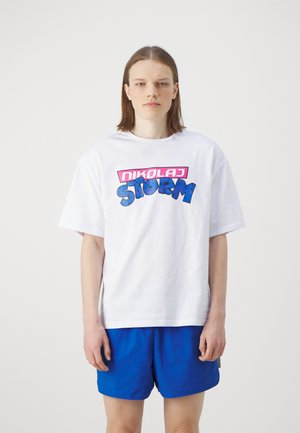 White cotton t-shirt featuring a colorful "NIKOLAJ STORM" graphic in pink and blue. Boxy fit with short sleeves, worn with blue shorts.