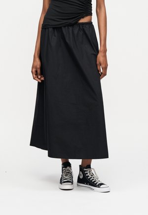 Άτομο που φοράει μαύρη μίντι φούστα με ελαστική μέση και μαύρα παπούτσια τύπου high-top με λευκά κορδόνια και σόλες.